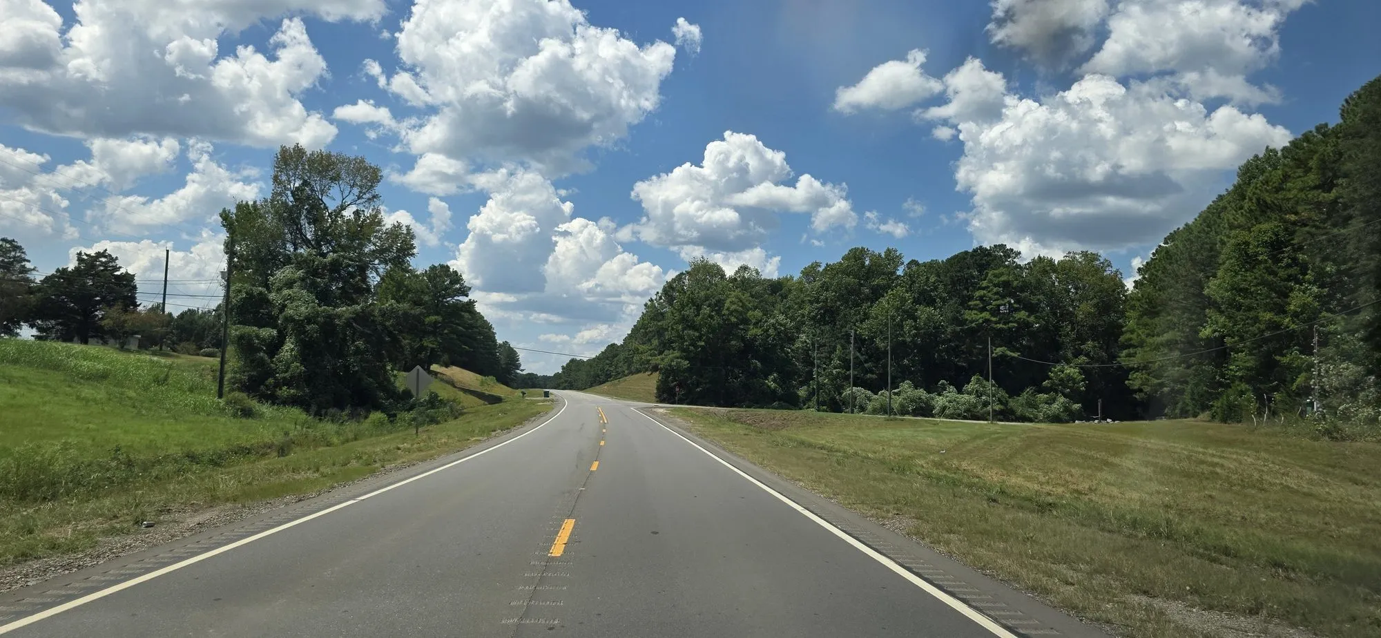 Two-lane highway running out of Brookwood between wooded ridges